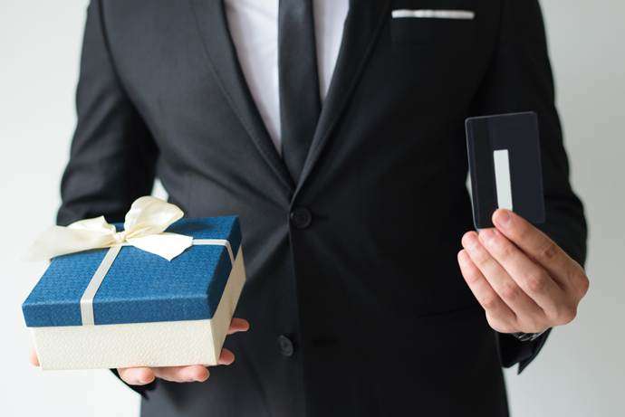 Person in a suit holding a blue wrapped gift box and a card, representing rewards and incentives